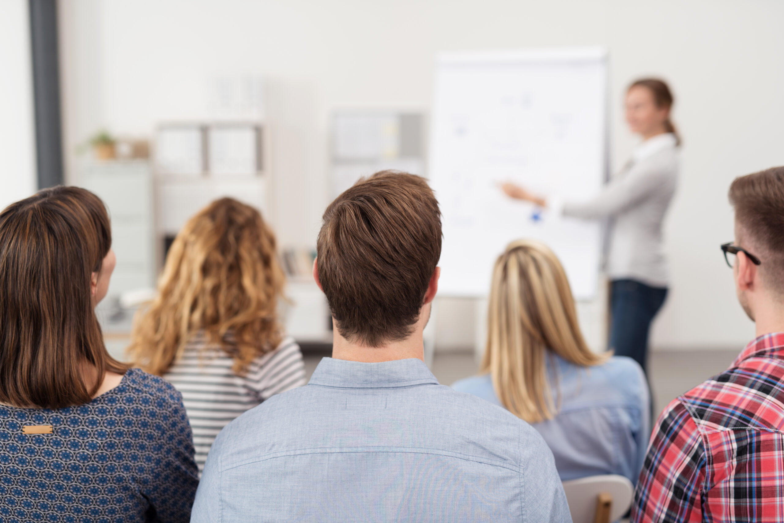 Teilnehmer einer Schulung oder Präsentation, die einer Dozentin zuhören, die vor einem Flipchart präsentiert Teilnehmer einer Schulung oder Präsentation, die einer Dozentin zuhören, die vor einem Flipchart präsentiert